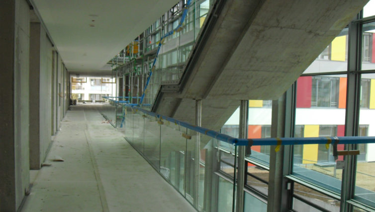 Innenaufnahme des Förderzentrums München Süd nach Fertigstellung des Rohbaus. Zu sehen ist der lange Flur und rechts die Treppe in das nächste Stockwerk aus Stahlbeton.